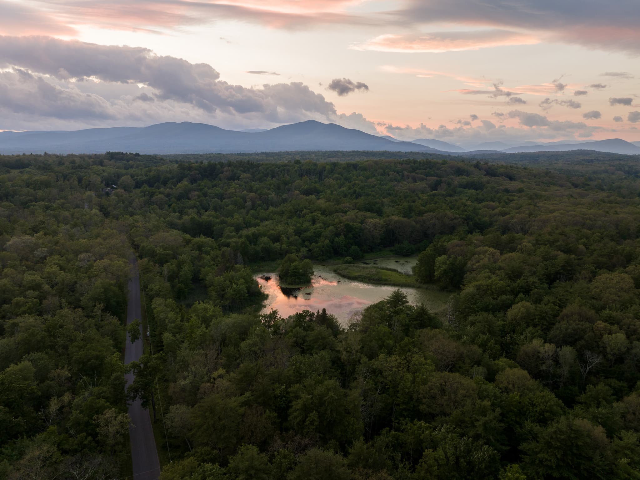 beautiful drone shot of a large darkly painted house nestled in woods with the Catskills in the background